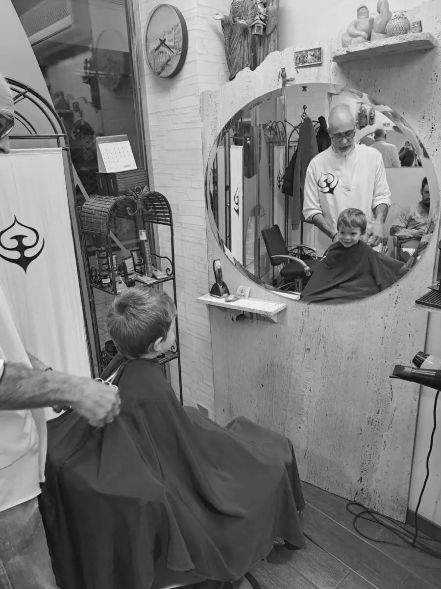 Gonzalo cortando el pelo a un niño frente al espejo de su peluquería en Logroño